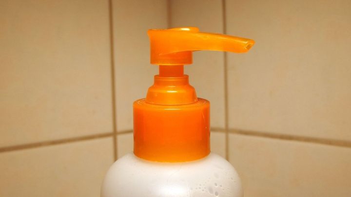 Ein Seifenspender mit orangener Pumpe steht auf einer Fliese und ist bereit, Duschgel oder Haarwaschmittel auszugeben.