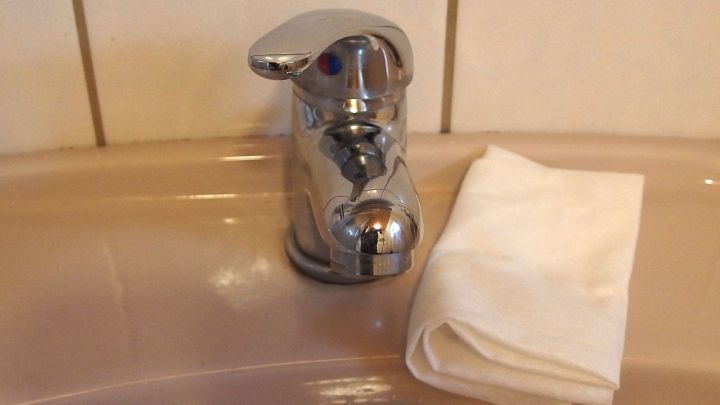 Ein verkalkter Wasserhahn steht auf einem Waschbecken, daneben liegt ein Reinigungstuch f&uuml;r die Pflege.