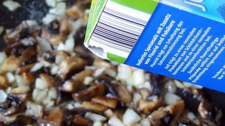 In einer Pfanne braten knackige, crosse Pilze mit Zwiebeln, w&auml;hrend eine Fl&uuml;ssigkeit aus einem Karton dar&uuml;ber gegossen wird.