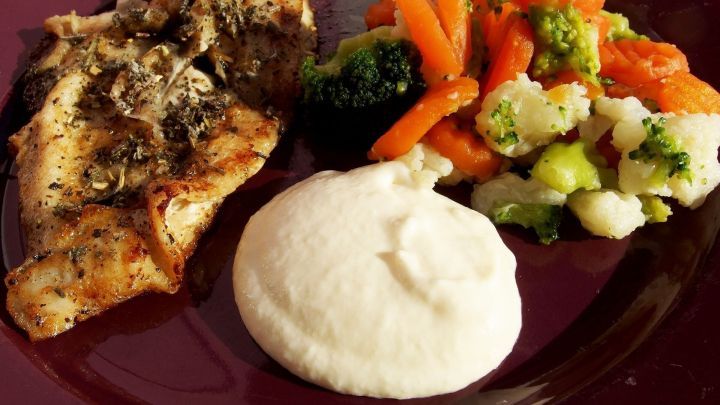 Ein geh&auml;uftes St&uuml;ck Meerrettichsahne liegt auf einem Teller neben gegrilltem Fisch und bunter Gem&uuml;semischung.