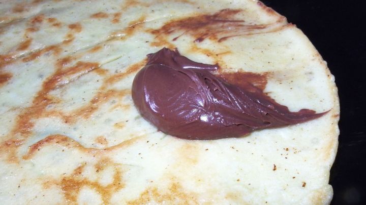 Eine goldbraune Pfannkuchenoberfl&auml;che hat einen Klecks selbstgemachter Nutella, der darauf geschmolzen ist, und wartet auf Genuss.