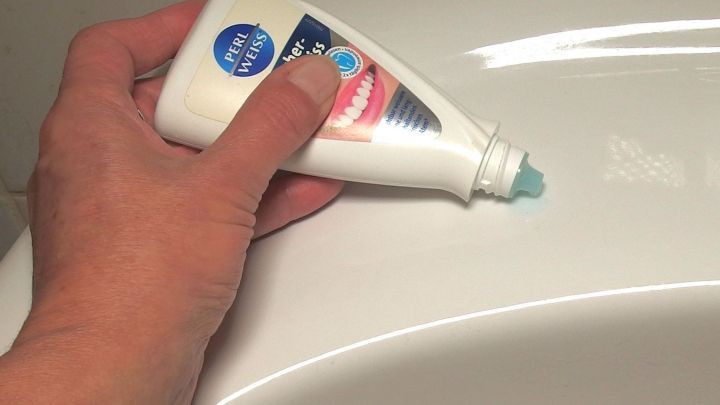 Eine Hand h&auml;lt eine Tube Reinigungsmittel, w&auml;hrend sie Rostflecken auf einer Badkeramik-Oberfl&auml;che entfernt.