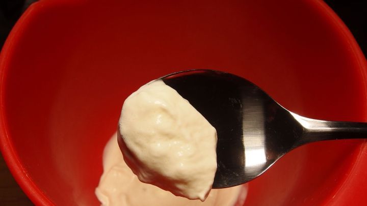 Ein L&ouml;ffel mit geschlagener Sahne wird in eine rote Sch&uuml;ssel gehalten, um die Zubereitung zu zeigen.
