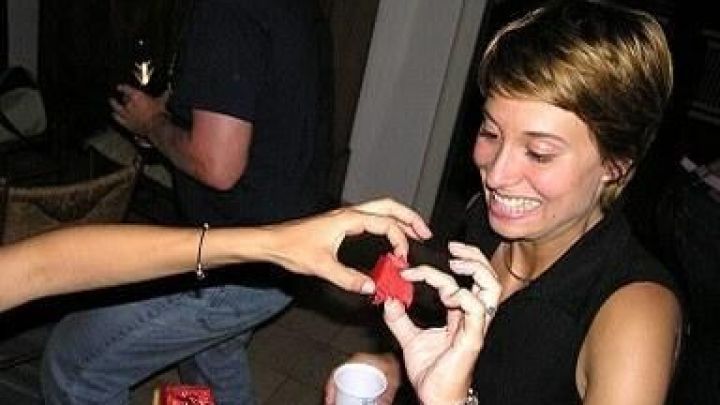 Frau freut sich &uuml;ber Wassermelonenst&uuml;ck von einer anderen Person in einer fr&ouml;hlichen Partyatmosph&auml;re mit Getr&auml;nken.