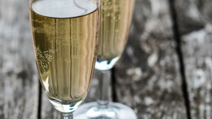 Zwei Gl&auml;ser mit sprudelndem Apfelsaft stehen auf einer rustikalen Holztischplatte und spiegeln sanftes Licht wider.