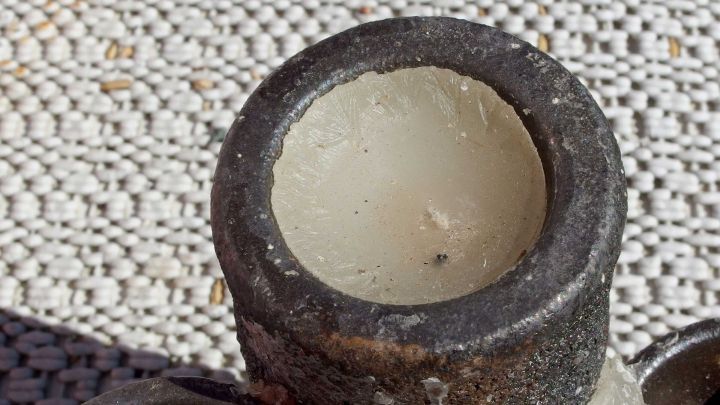 Ein Kerzenst&auml;nder wird von Wachsresten befreit, w&auml;hrend er auf einer strukturierten Unterlage steht.