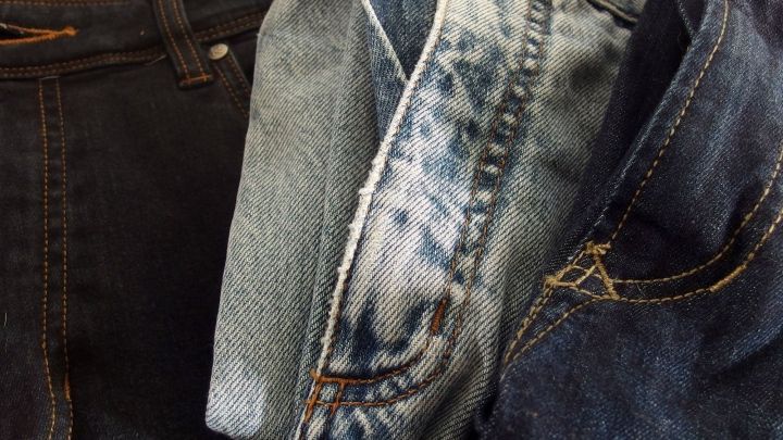 Jeans werden &uuml;bereinander gestapelt, wobei eine stark gewaschene Jeans in der Mitte und dunklere Jeans an den Seiten zu sehen sind.