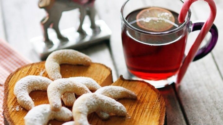 Vanillekipferl liegen auf einem rustikalen Holzbrett, w&auml;hrend ein Glas Tee daneben steht. Ein Rentier dekoriert die Szenerie.