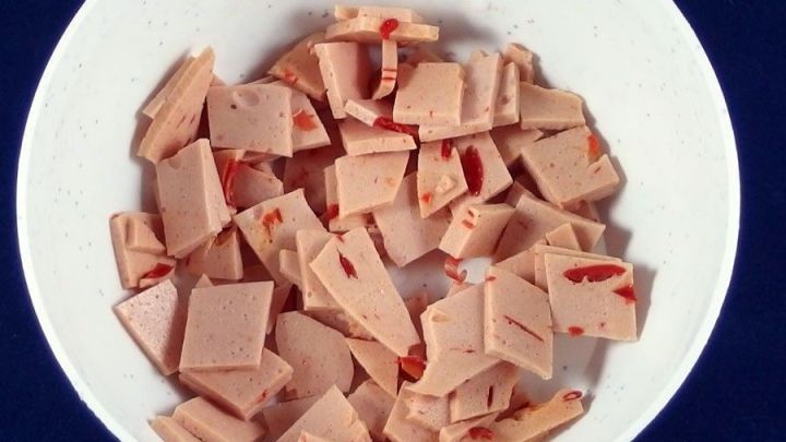 Kleine St&uuml;cke von Wurst liegen in einer wei&szlig;en Sch&uuml;ssel, auf einem blauen Hintergrund, bereit zum Verzehr oder f&uuml;r Rezepte.
