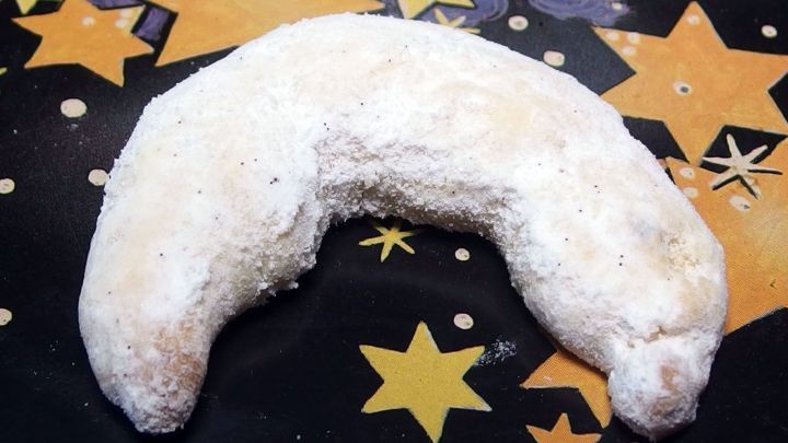 Ein Vanillekipferl liegt auf einem bunten, sternenf&ouml;rmigen Teller und strahlt s&uuml;&szlig;es Weihnachtsgeb&auml;ck-Ambiente aus.