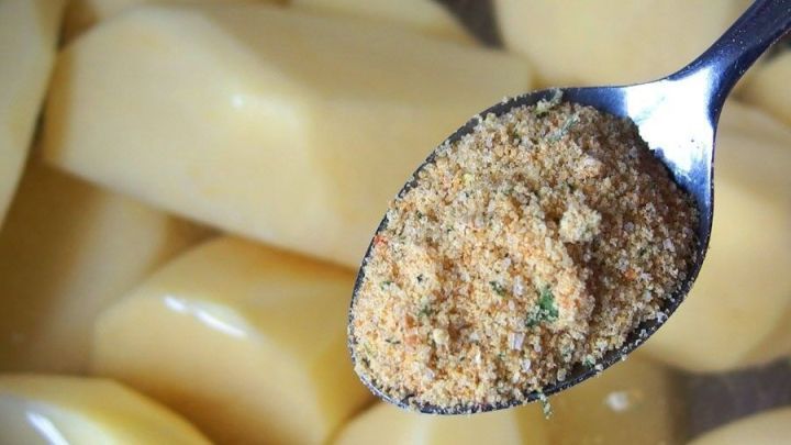 Ein L&ouml;ffel mit einer salzfreien Gew&uuml;rzmischung schwebt &uuml;ber rohen, gesch&auml;lten Kartoffeln in einem Topf.