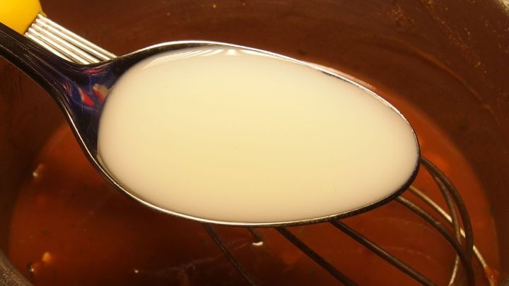 Ein L&ouml;ffel mit einer wei&szlig;en Fl&uuml;ssigkeit &uuml;ber einer Sch&uuml;ssel, w&auml;hrend man So&szlig;e verfeinert, um den Geschmack zu verbessern.