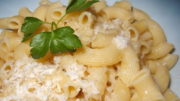 Nudeln mit geschmolzener Butter und Parmesan sind auf einem wei&szlig;en Teller angerichtet, garniert mit frischen Kr&auml;utern.