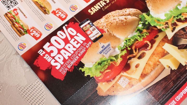 Ein Werbeflyer zeigt ein gro&szlig;es Burger-Angebot mit dem Text &bdquo;50% SPAREN&ldquo; und bezieht sich auf spezielle Gutscheine.
