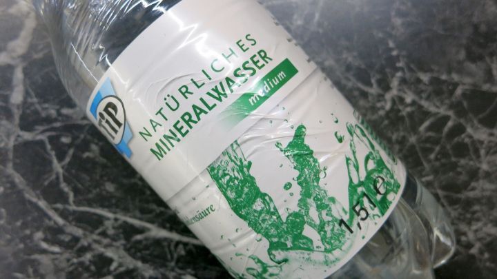 Flasche mit "Tip Nat&uuml;rliches Mineralwasser medium" liegt auf einer dunklen Marmoroberfl&auml;che. Text: "Mit Kohlens&auml;ure".