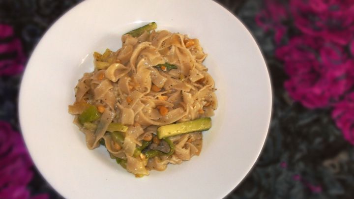 Zucchini Bandnudeln sind in einer wei&szlig;en Schale angerichtet, umgeben von buntem Hintergrund, der eine lebendige Atmosph&auml;re schafft.