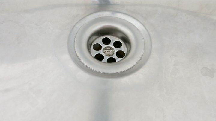 Ein metallener Ausguss mit L&ouml;chern im Abfluss, umgeben von einer glatten, silbernen Oberfl&auml;che, wirkt sauber und unbenutzt.