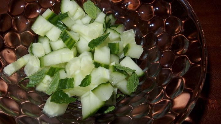 Ein frischer Gurkensalat liegt ansprechend in einer durchsichtigen Sch&uuml;ssel, gew&uuml;rfelt und mit Minze garniert.
