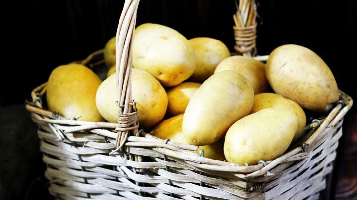 Ein Korb mit frischen Kartoffeln liegt auf einem dunklen Holzuntergrund und wartet darauf, verwendet zu werden.