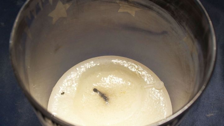 Ein Kerzenglas ist mit einer fast abgebrannten Kerze gef&uuml;llt und steht auf einem Tisch in einem gem&uuml;tlichen Raum.