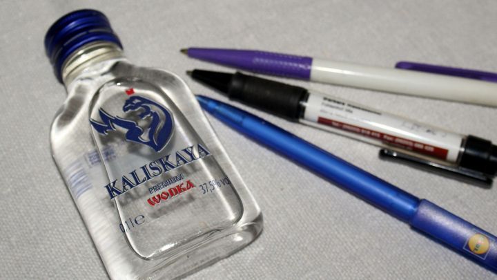 Eine Wodkaflasche liegt neben mehreren Kugelschreibern auf einer Oberfl&auml;che, bereit, um Flecken zu entfernen.