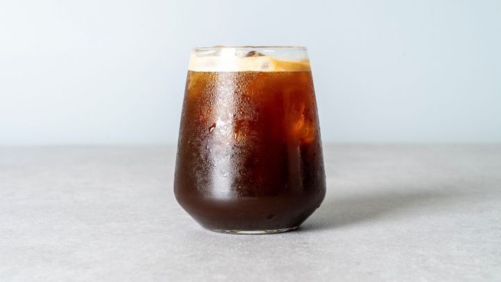 Ein Glas Berentzen mit Cola steht auf einer grauen Oberfl&auml;che. Das Getr&auml;nk hat eine dunkle Farbe und ist mit Eisw&uuml;rfeln gef&uuml;llt.