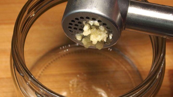 Eine Knoblauchpresse dr&uuml;ckt frischen Knoblauch in ein Glas, bereit zur sofortigen Verwendung in der K&uuml;che.
