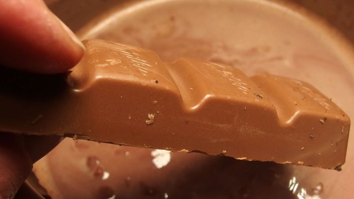 Eine Hand h&auml;lt ein St&uuml;ck Schokolade &uuml;ber einer Sch&uuml;ssel mit k&ouml;stlichem Schokoladenpudding, der cremig aussieht.