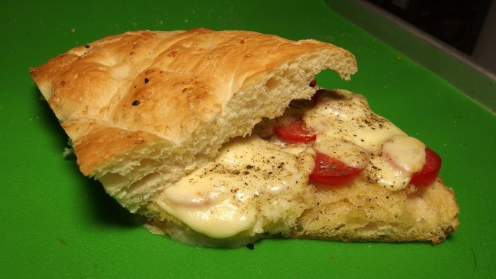 Ein D&ouml;ner mit Tomate und Mozzarella liegt auf einem gr&uuml;nen Brett, aufgeschnitten und bereit zum Genuss.