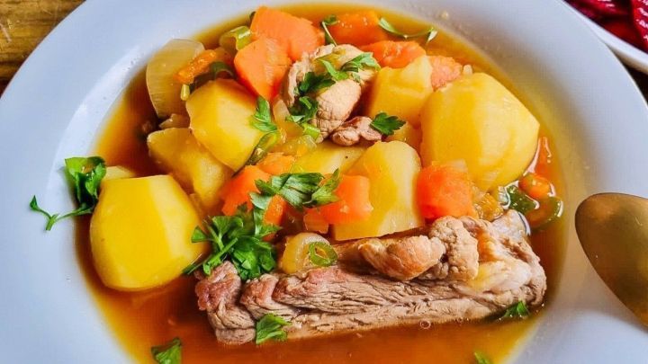 Eine anschauliche M&ouml;hrensuppe mit Kassler, gef&uuml;llt mit Kartoffeln, Karotten und frischen Kr&auml;utern in einer wei&szlig;en Sch&uuml;ssel.