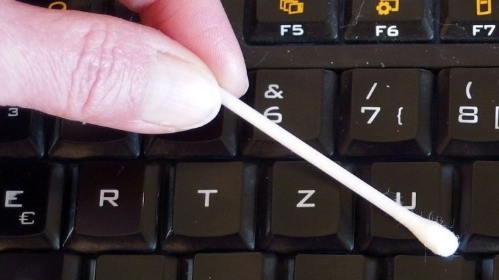 Ein Q-Tip reinigt die Tasten einer Computertastatur, um Schmutz zu entfernen. Hintergrund ist eine dunkle Tastatur.