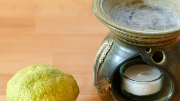Eine Duftlampe steht auf einem Holzuntergrund und wird mit Zitronensaft gereinigt; daneben liegt eine frische Zitrone.