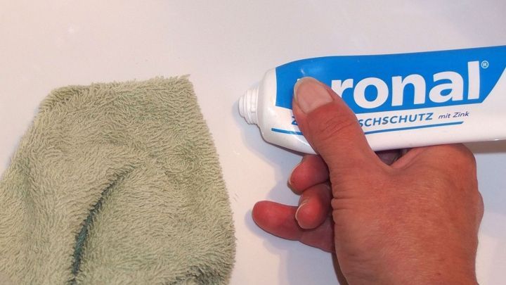 Ein Hand h&auml;lt eine Tube Zahnpasta und dr&uuml;ckt sie auf ein gr&uuml;nes Tuch, um Flecken in der Badewanne zu entfernen.