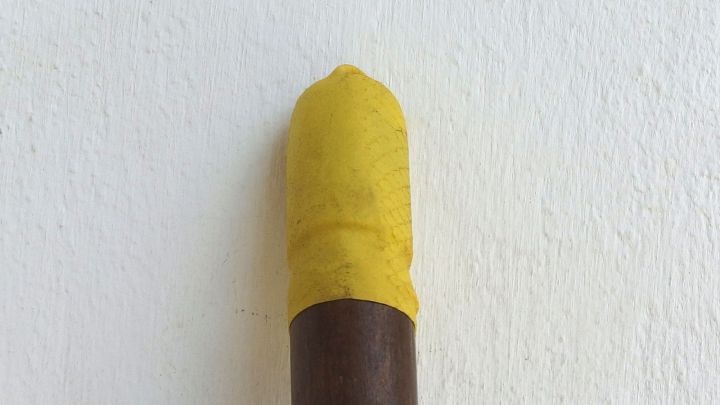 Ein Besen steht senkrecht in der Ecke, sein Griff ber&uuml;hrt die Wand, w&auml;hrend die gelbe Spitze oben sichtbar ist.