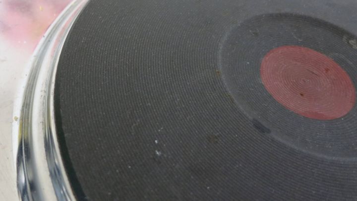 Eine schwarze Herdplatte zeigt R&uuml;ckst&auml;nde und Verschmutzungen, w&auml;hrend sie gereinigt wird. Der Hintergrund ist verschwommen.