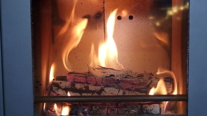 Ein Kaminglas zeigt lebendige Flammen, die Holzscheite verbrennen, und bildet einen warmen, gem&uuml;tlichen Hintergrund.