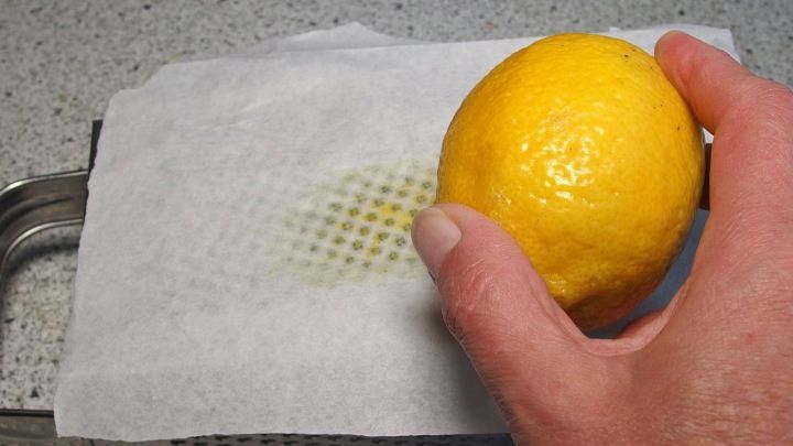 Eine Hand h&auml;lt eine Zitrone &uuml;ber Butterbrotpapier, w&auml;hrend die Schale gerieben wird, um l&auml;stiges Putzen zu vermeiden.