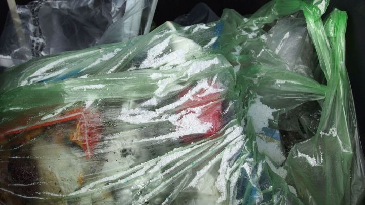 Ein Plastikm&uuml;llsack ist halb gef&uuml;llt mit Abf&auml;llen und ist in einem engen, dunklen M&uuml;llcontainer. Das Bild verdeutlicht M&uuml;llentsorgung.