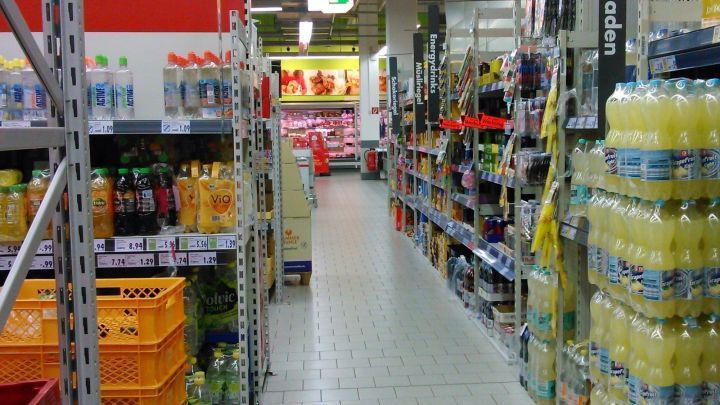 Regale im Supermarkt stehen ordentlich nebeneinander, w&auml;hrend Kunden durch den Gang gehen und Produkte ausw&auml;hlen.