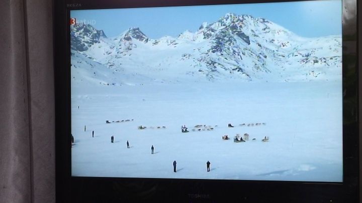 Ein Fernseher zeigt eine schneebedeckte Landschaft mit Menschen, die sich im Winter am Berg bewegen.