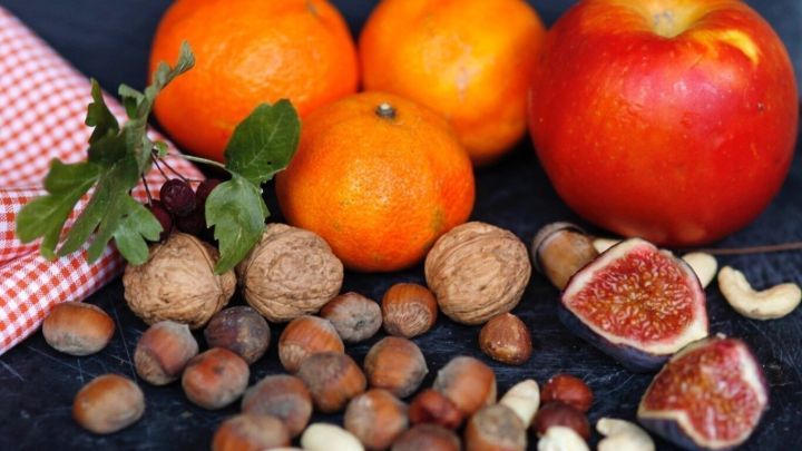 Frisches Obst und N&uuml;sse liegen auf einem dunklen Hintergrund, w&auml;hrend die N&uuml;sse und Feigen bunt verteilt sind.