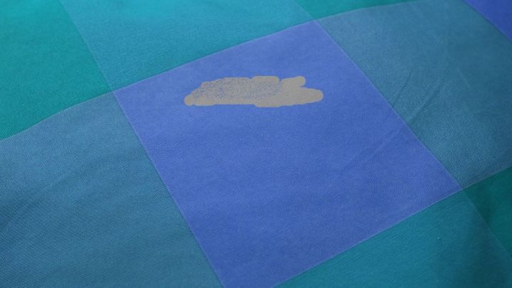 Auf einem bunten, gemusterten Stoff ist ein Make-up-Fleck sichtbar, der entfernt werden soll.