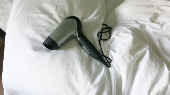 Ein Haartrockner liegt auf einem Bett mit einem Federkissen, um es wieder fluffig und luftig zu machen.