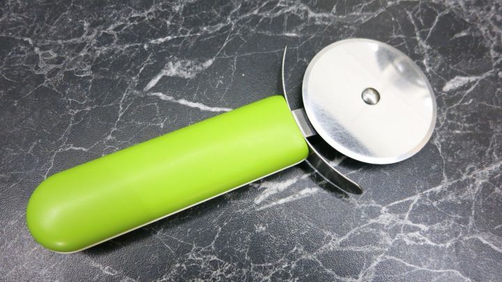 Ein gr&uuml;ner Pizzaschneider liegt auf einer schwarzen Marmorplatte und eignet sich zum einfachen Schneiden von Blechkuchen.