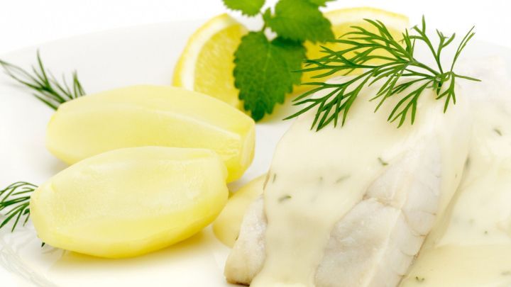 Auf dem Teller liegt ein Karpfenfilet in cremiger So&szlig;e, umgeben von Kartoffeln und frischen Kr&auml;utern, Zitrone ist dekorativ platziert.