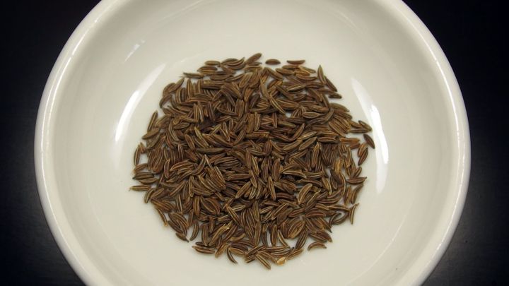 K&uuml;mmelsamen liegen in einer wei&szlig;en Sch&uuml;ssel, umgeben von einem schwarzen Hintergrund, bereit zur Verwendung gegen Bl&auml;hbauch.