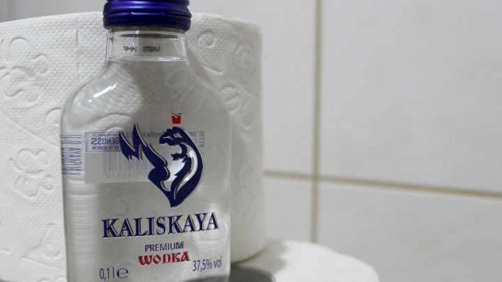 Eine Flasche Wodka steht auf einem Toilettenpapierstapel in einem Badezimmer, was auf einen m&ouml;glichen Durchfall hinweist.