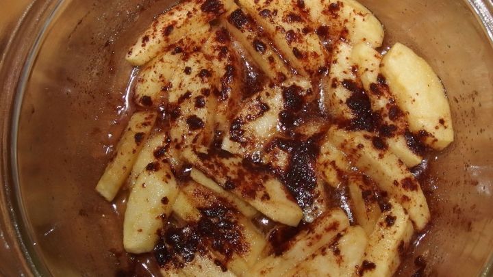 Gebackene Apfelst&uuml;cke liegen in einer Glasform und sind leicht karamellisiert, umgeben von einem k&ouml;stlichen Zimtgeruch.