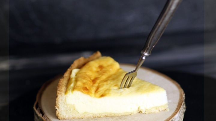 Ein K&auml;sliceh durch Haube mit der Alufolie auf einem Holzbrett liegt bereit, w&auml;hrend eine Gabel darauf zeigt.