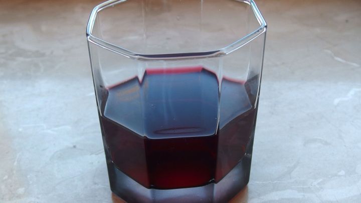 Ein Glas mit dunkelrotem Johannisbeersaft steht auf einer hellen Oberfl&auml;che und wartet darauf, getrunken zu werden.